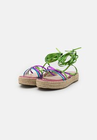 Sandales espadrilles avec une semelle en jute, présentant un design de lanières métalliques colorées en vert et violet, avec des accents torsadés pour la fixation.