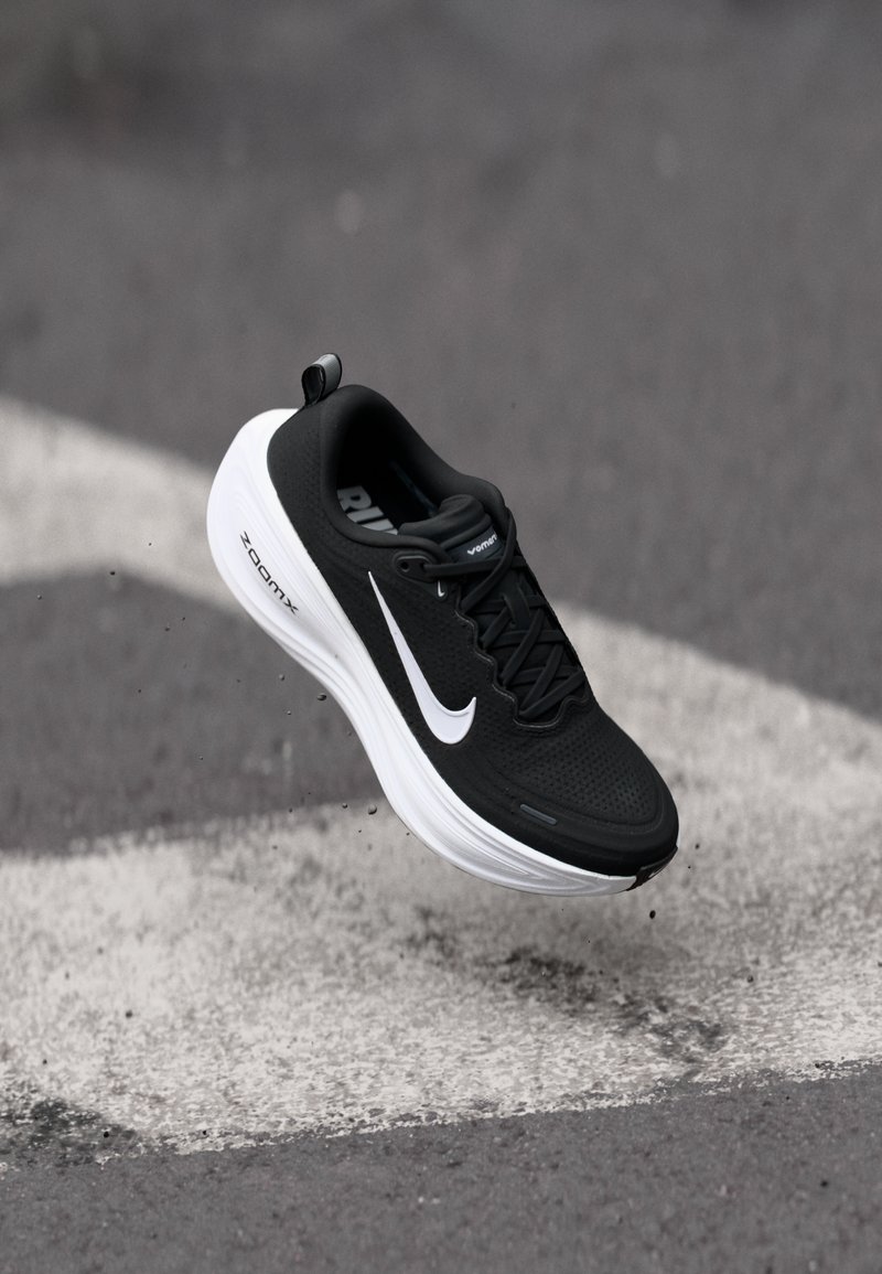 Juoda bėgimo batai su tekstūruotu paviršiumi, baltas Nike swoosh ir paminkštinta, kreivos formos balta padas. Yra raišteliai ir kilpelė kulne.
