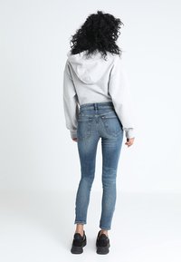 Sudadera gris con capucha con cordón, combinada con jeans ajustados azules. El conjunto se complementa con deportivas negras de superficie texturizada.