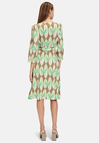 Braun gemustertes Kleid mit grünen und hellrosa geometrischen Formen, Dreiviertelarm, Taillengürtel und knielanger Säume.