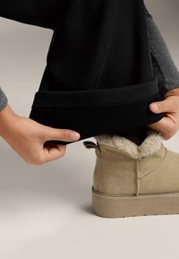 Crna majica dugih rukava s podvrnutim manžetama koju ruke podešavaju, uparen s smeđim antilop čizmama s mekanim unutarnjim slojem i debelim potplatom.