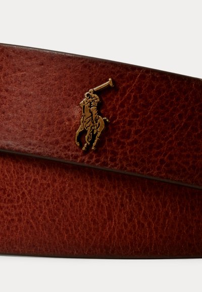 Pruun tekstuuriga nahast vööosa, mille ääre lähedal on väike kuldne polo mängija embleem heledal taustal embosseeritud.