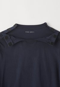 Navy blue cotton t-shirt featuring a round neckline, soft texture, and two snap closures at the shoulder. "PIER · ONE" logo printed inside.