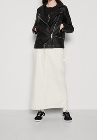 Czarna skórzana kurtka motocyklowa z srebrnymi zamkami, noszona na czarnej koszulce, w połączeniu z białą spódnicą do kostek i czarnymi sneakersami.