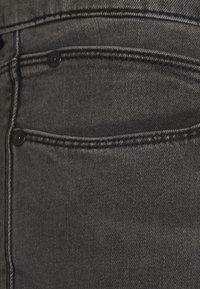 Zbliżenie na czarną tkaninę dżinsową z widocznym ściegiem i metalowymi nitami na tylnej kieszeni.