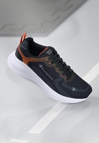 Black athletic shoe with orange accents, mesh upper, padded collar, and thick white sole. Features logo on side and tongue, and lace-up design.