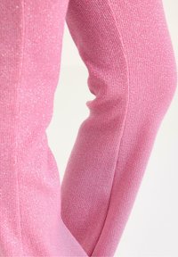 Lyserøde ribstrikkede leggings med en metallisk glans. Teksturen er blød med et tætsiddende design, der fremhæver former og en let skinnende overflade.