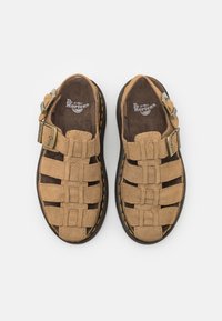 Brune semskede sandaler med et sammenflettet stropdesign, justerbar spænde og sort gummisål med gule stikninger.