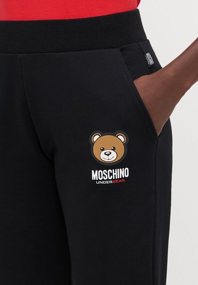 Crne trenirke sadrže izvezeni logo medvjeda i tekst "MOSCHINO UNDERBEAR". Pojas je elastičan i ima bočne džepove za praktičnost.