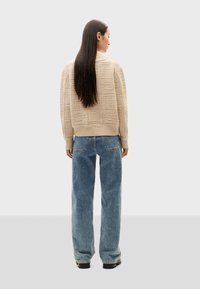 Pull en beige texturé avec un col rond, un ourlet côtelé et des manches longues, associé à un jean droit bleu clair ample.