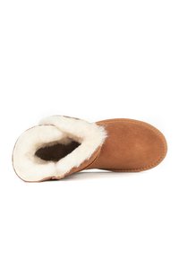 Bota de ante marrón con un suave forro de pelo blanco, forma redondeada y adornos cosidos a lo largo de la costura. El interior es suave y acogedor.