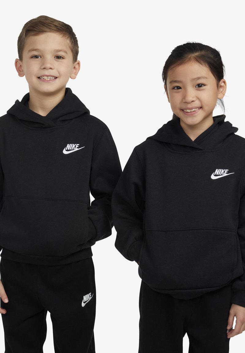Fekete kapucnis pulóverek, elülső zsebekkel, fehér Nike logóval a mellkason. Hozzá illő fekete nadrággal viselve. Puha anyag és laza szabás.