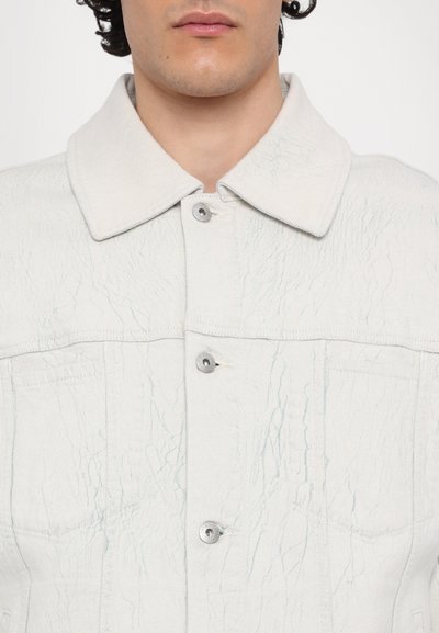 Giubbino in denim grigio chiaro con una texture stropicciata, grande colletto, sei bottoni e due tasche frontali. Presenta dettagli con bottoni metallici.