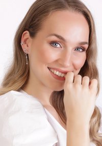 Pendientes de plata con diseño de estrellas y colgantes, adornados con piedras preciosas transparentes. Llevados por una modelo con cabello largo, frente a un fondo claro.