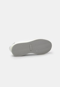 Sneaker bianco con suola in gomma testurizzata, caratterizzata da un motivo di presa ondulato, e un design superiore liscio con minime accentuazioni nere vicino alla punta.
