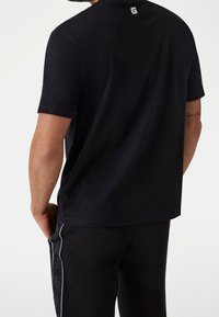 Černé tričko s měkkou strukturou, krátkými rukávy a kulatým výstřihem. Na zadní straně má malé logo a je stylizováno s černými kalhotami.