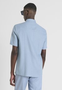 Câmara azzurra a maniche corte con colletto, caratterizzata da una leggera texture e un piccolo dettaglio posteriore vicino al collo. Abbinata a pantaloni coordinati.
