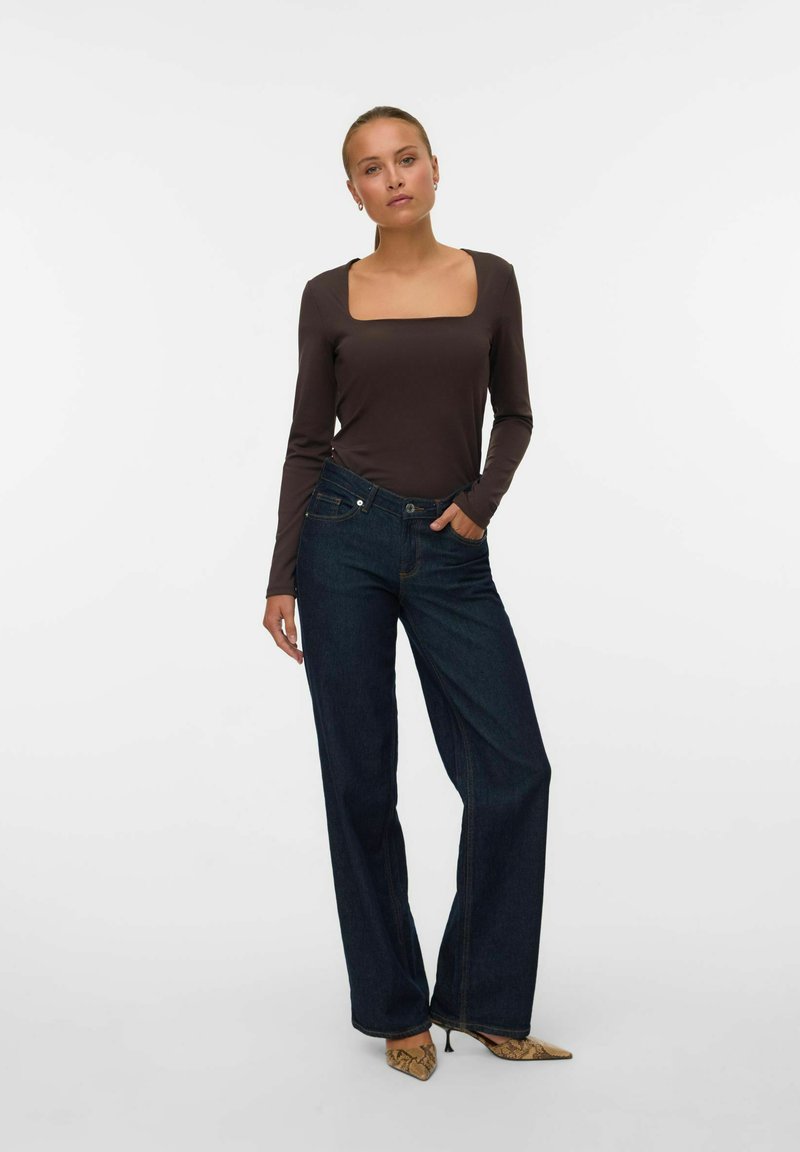 Bruine lange mouw top met een vierkante halslijn, gecombineerd met donkerblauwe wijde jeans. Het model draagt puntige hakken met slangenprint.