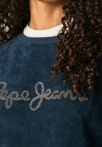 Navy blue sweatshirt with a soft texture featuring silver glittery "Pepe Jeans" lettering across the chest and a crew neckline.