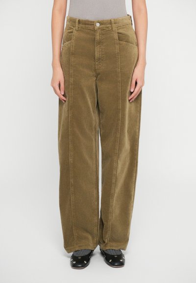 Pantalons larges en velours côtelé de couleur vert olive avec un tissu texturé, poches avant et fermeture avec bouton ; assortis à des sabots noirs et des chaussettes grises.