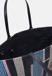 Tote-väska med ett vävt mönster av blå, röda och krämfärgade ränder, med svarta syntetläderremmar och ett blixtlåsförsedd inre ficka.