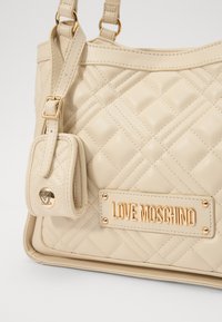 Bež torba za ramena iz veštačke kože, sa zlatnim detaljima, pločicom "LOVE MOSCHINO" i odvojivom bočnom tašnom.