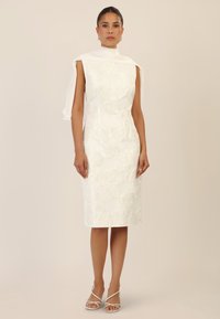 White dress with floral embossed texture, sleeveless design, high neckline, and an attached fabric shawl draped over one shoulder.
