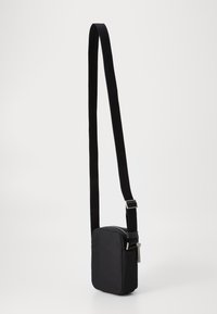 Černá crossbody taška vyrobená z hladkého materiálu, obdélníkového tvaru, s vybavením na zip a nastavitelným popruhem s kovovou sponou.