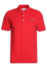 Červené polo tričko s texturovanou látkou, trojknopovým zapínáním a zeleným logem Lacoste na hrudi. Krátké rukávy a klasický střih.