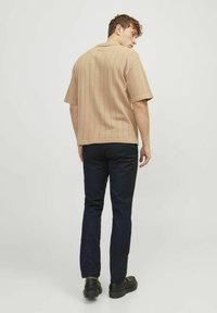 Beige ribbed short-sleeve shirt with a straight hem, worn with dark navy trousers and black shoes, viewed from the back.
