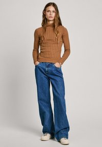 Brun ribbad långärmad topp med hög halsringning, kombinerad med lösa blå denimjeans och vita sneakers. Outfiten inkluderar sidofickor.