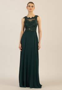 Langes smaragdgrünes Kleid mit einem durchsichtigen, bestickten Mieder mit floralen Details und einem glatten, fließenden Rock, der bis zum Boden reicht.