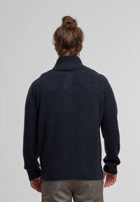 Dark navy wool sweater with a high collar, ribbed cuffs, and hem, featuring a soft texture and minimal design, viewed from the back.