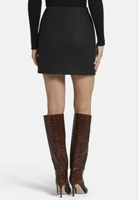 Jupe mini grise avec une texture lisse et une fermeture éclair dans le dos, associée à des bottes à talons hauts brillantes marron, montant jusqu'au genou, avec un motif crocodile.