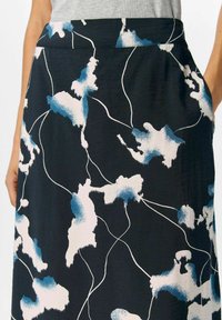 Une jupe noire ornée de motifs abstraits bleus et blancs, fabriquée en tissu doux, avec une texture lisse et des poches latérales.