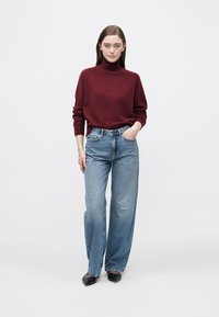 Pull col haut bordeaux, texture en maille moyenne ; jean bleu clair à jambes larges avec légère usure ; chaussures noires à bout pointu.