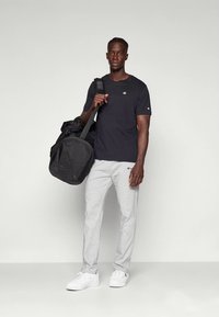 Črna majica s kratkimi rokavi, sive hlače za vadbo, beli športni copati in črna športna torba. Preprost dizajn brez vzorcev ali opazne opreme.