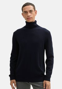 Ciemnogranatowy sweter z golfem wykonany z prążkowanej dzianiny, z długimi rękawami i dopasowanym fasonem. Brak wyraźnych wzorów lub elementów ozdobnych.