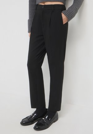 Pantalons noirs ajustés avec une texture lisse, dotés d'un devant plat, de poches latérales et d'une coupe slim. Portés avec des mocassins brillants.