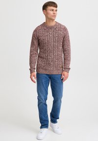 Pull en tricot bordeaux avec un motif en côtes texturé, associé à un jean bleu clair et des baskets blanches. Il a un col rond.