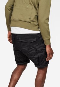 Svarta cargoshorts med fickor och uppvikta muddar, gjorda av slitstark tyg. Kombinerat med en grön sweatshirt och vit T-shirt.