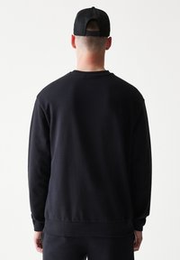 Μαύρο φούτερ με στρογγυλή λαιμόκοψη από απαλό ύφασμα. Διαθέτει ριμπ μανσέτες και τελείωμα, με καθαρό, μινιμαλιστικό σχέδιο. Εμφανίζεται από πίσω.