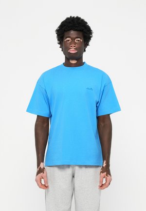 Blå bomulds t-shirt med rund halsudskæring og korte ærmer, prydet med et lille sort logo på brystet. Grå sweatpants fuldender outfittet.