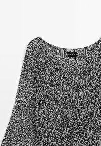 Black and white knitted sweater with a wide neckline and three-quarter sleeves, featuring a textured, loose weave pattern.