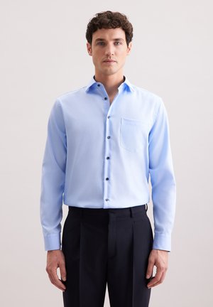 Camicia azzurra a maniche lunghe con taschino, colletto button-down e bottoni a contrasto, abbinata a pantaloni scuri. Trama del tessuto liscia.