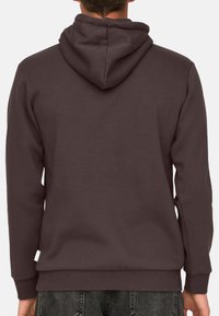 Mörkbrun hoodie med känguruficka och justerbar dragskohuva. Mjukt bomullsmaterial med en slät textur och ribbade ärmslut.