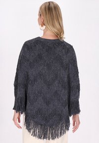 Maglione a maglia con frange di colore grigio scuro, caratterizzato da una vestibilità ampia, tessuto testurizzato e orlo arrotondato. Maniche lunghe con bordi sfilacciati.