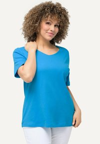 T-shirt turchese a maniche corte con scollo a V, realizzato in tessuto morbido con vestibilità comoda. Presenta un design semplice e una consistenza liscia, abbinato a pantaloni bianchi.