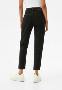 Jeans de mezclilla negro de cintura alta con corte recto, que cuentan con dos bolsillos traseros y una tela texturizada. Combinados con zapatillas blancas.