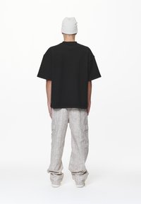 T-shirt nera oversize con spalle scese abbinata a pantaloni cargo grigi chiari con motif. Modello che indossa un berretto bianco, rivolto di spalle.